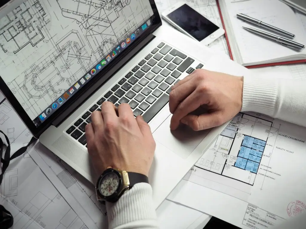 Architect reviewing detailed floor plans and schematics on a laptop with a smartphone nearby. CAD Freelancer Freelancer
